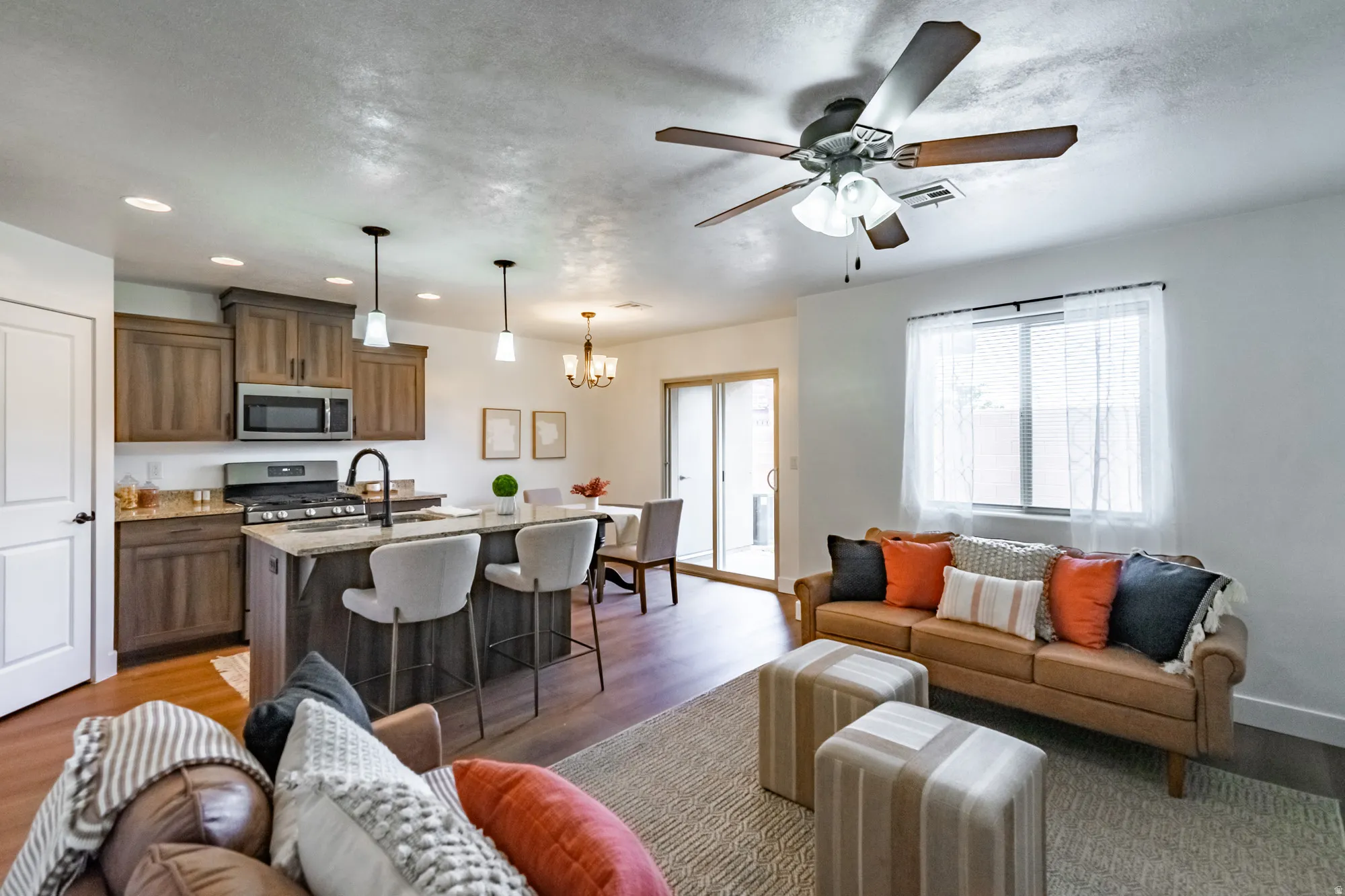 Open-concept living space featuring wood-finish flooring, a kitchen island with pendant lighting, stainless steel appliances, and a ceiling fan