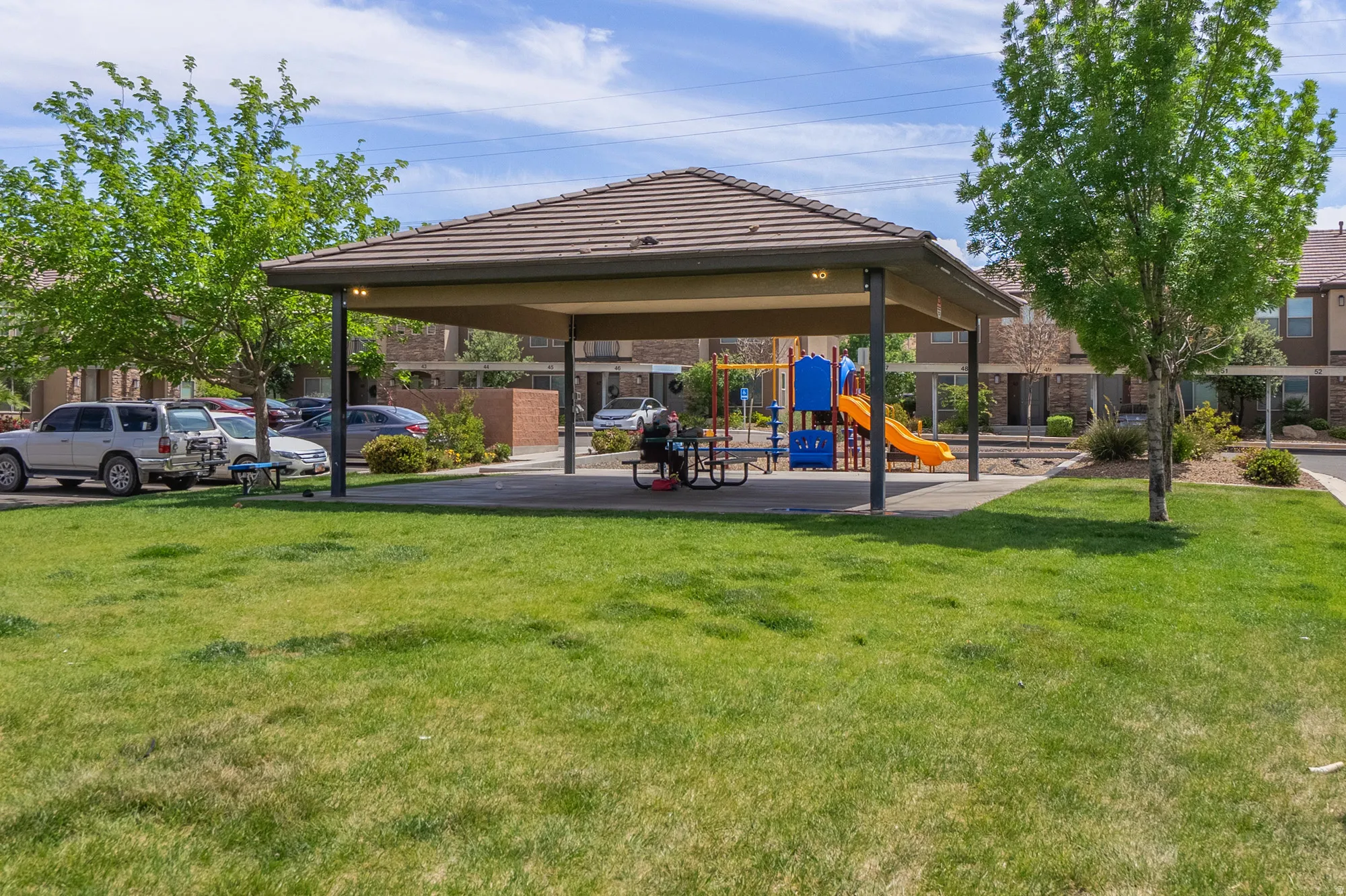 Community amenity area featuring a covered picnic structure with a tiled roof, an adjacent playground with colorful equipment, and surrounding green spaces