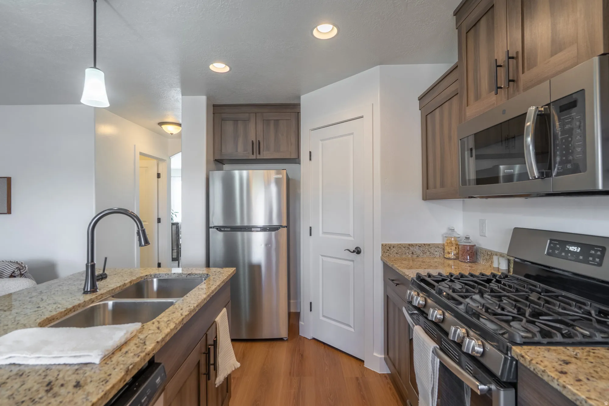 Open-concept kitchen featuring granite countertops, wood-finish flooring, stainless steel appliances, modern cabinetry, and recessed lighting