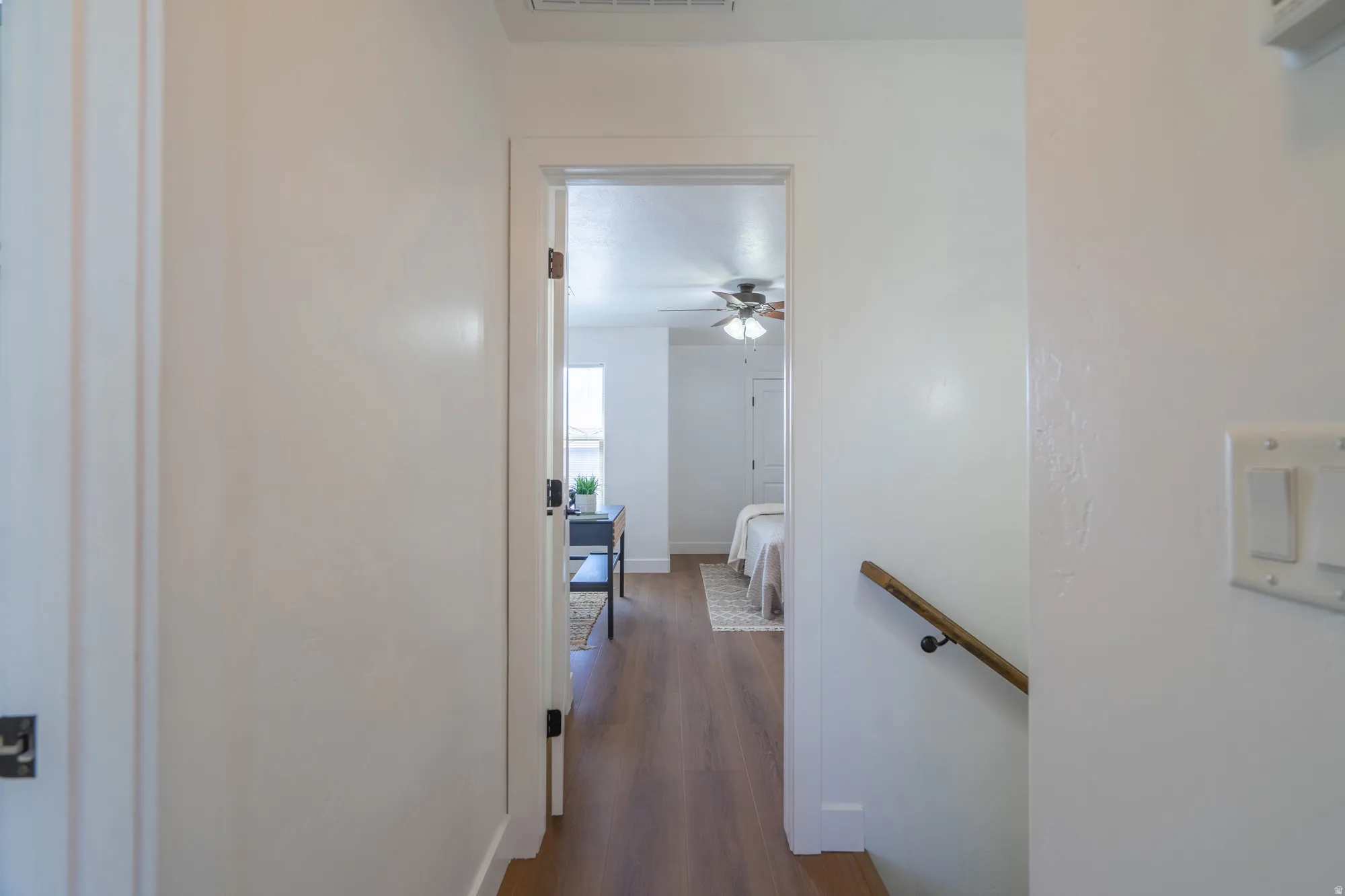 Hallway with wood-finish flooring, white walls, and a wooden handrail