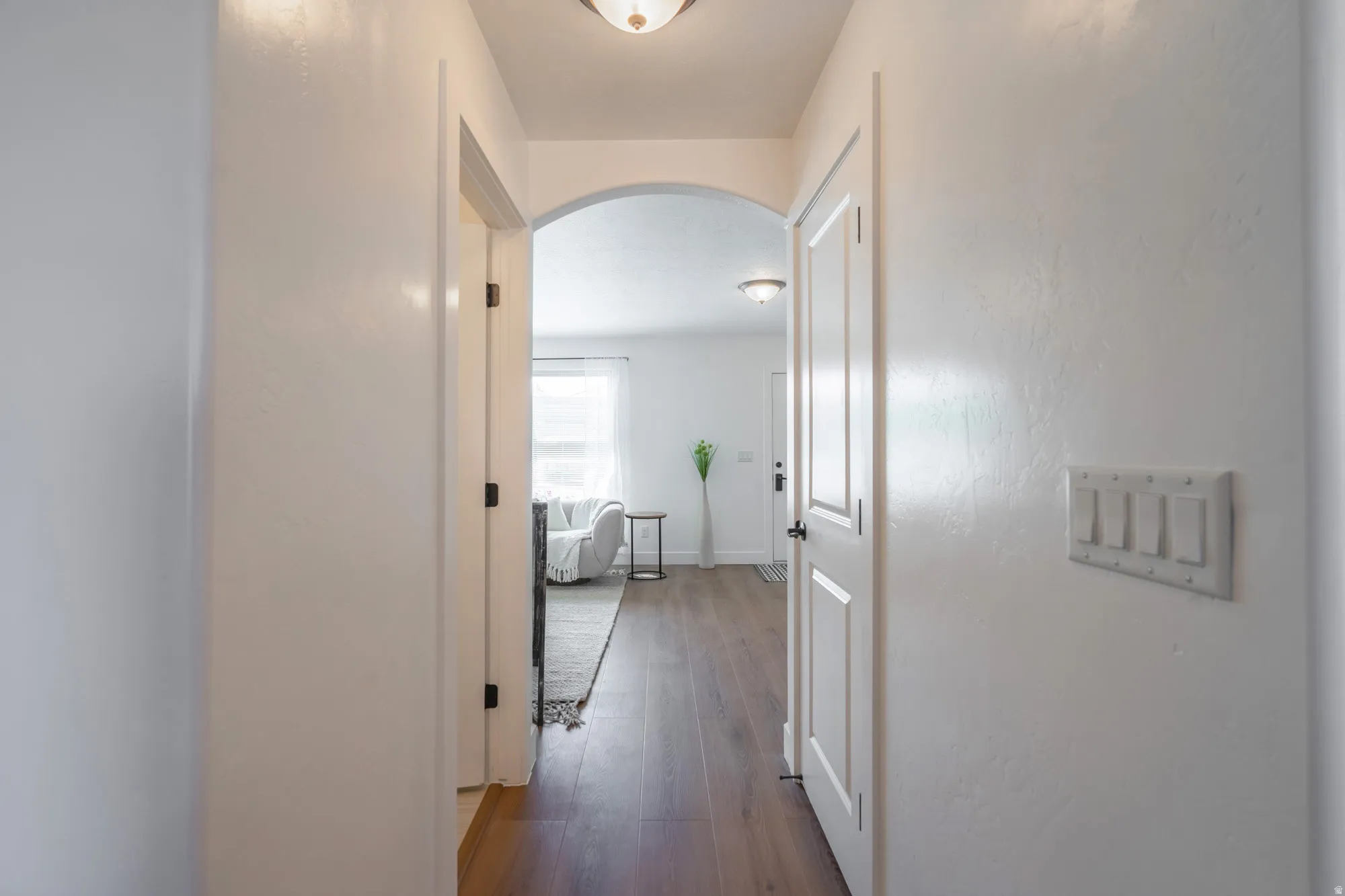 Hallway featuring wood-finish flooring, white paneled doors, an arched doorway, and overhead lighting fixtures