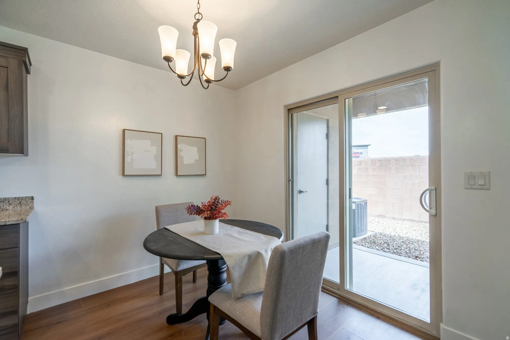 Dining area featuring wood-finish flooring, a contemporary chandelier, and a sliding glass door to an outdoor patio with a gravel landscape and block wall