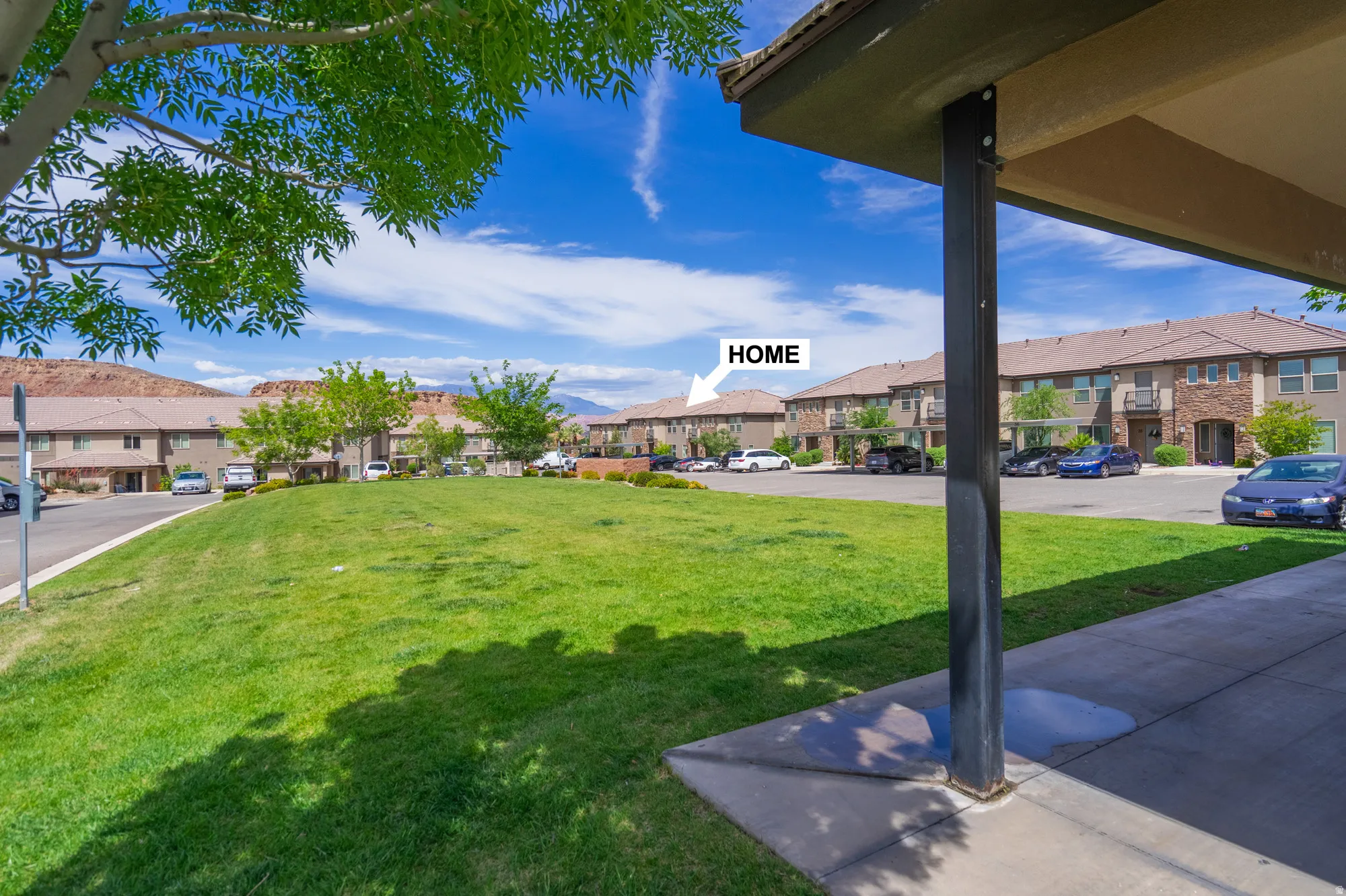 Expansive green space featuring a large lawn and mature trees, surrounded by multi-story residential buildings with tan exteriors and reddish-brown tile roofs