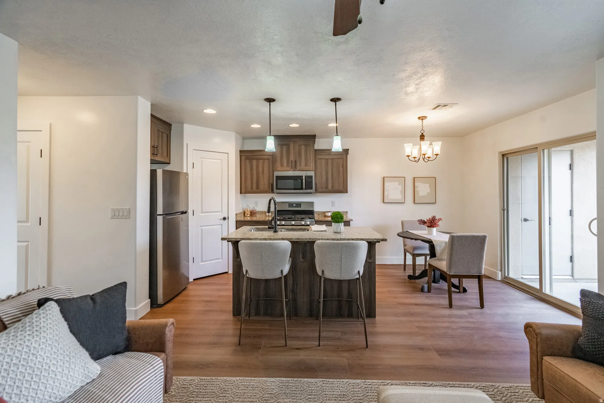 Open-concept living area featuring wood-finish flooring, a kitchen island with pendant lighting, stainless steel appliances, and sliding glass doors to outdoor space