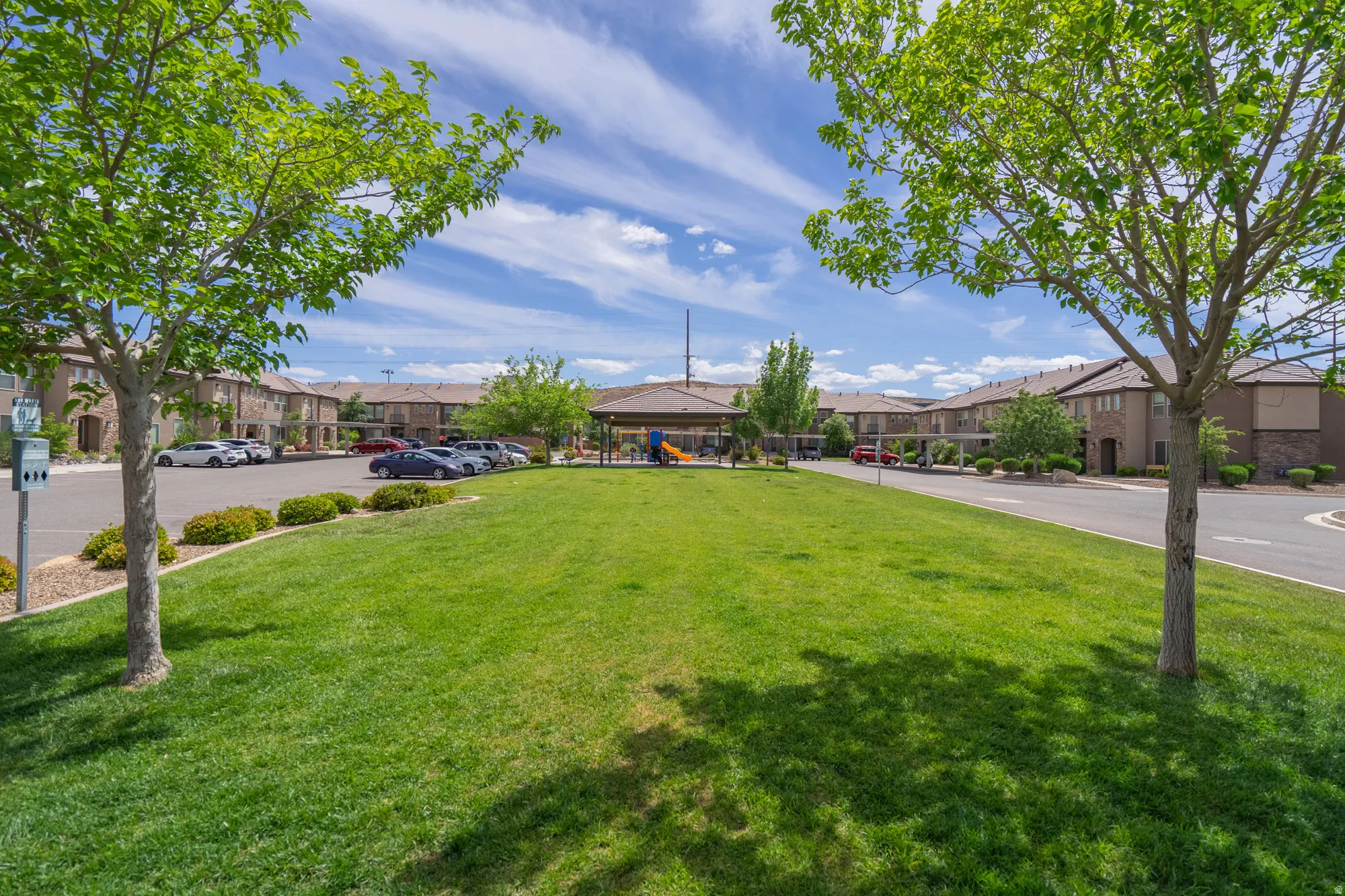 Expansive green lawn area featuring mature trees, a covered gazebo, and a play structure