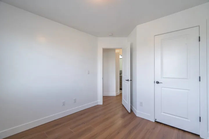Room with wood-finish flooring, white baseboards, and bright white walls