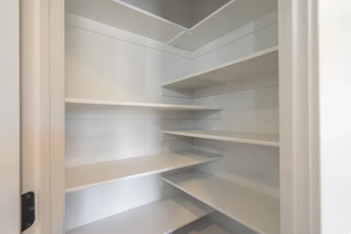 Corner pantry featuring multiple white shelves and white paneled walls
