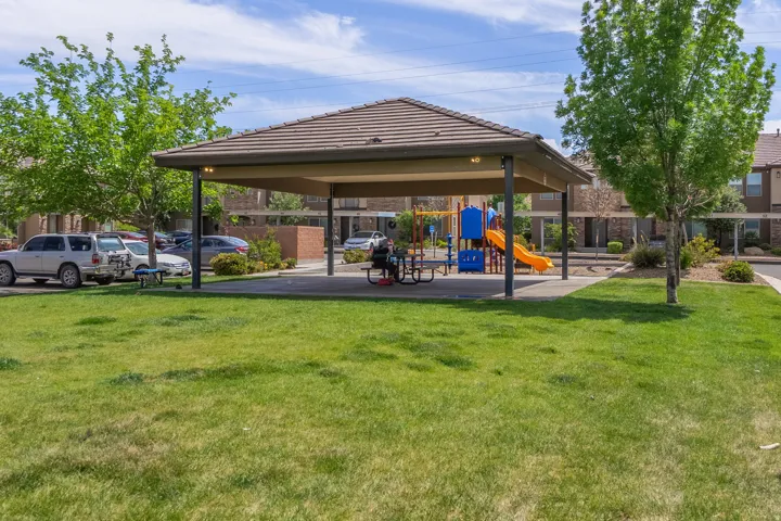 Community amenity area featuring a covered picnic structure with a tiled roof, an adjacent playground with colorful equipment, and surrounding green spaces