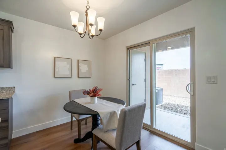 Dining area featuring wood-finish flooring, a contemporary chandelier, and a sliding glass door to an outdoor patio with a gravel landscape and block wall