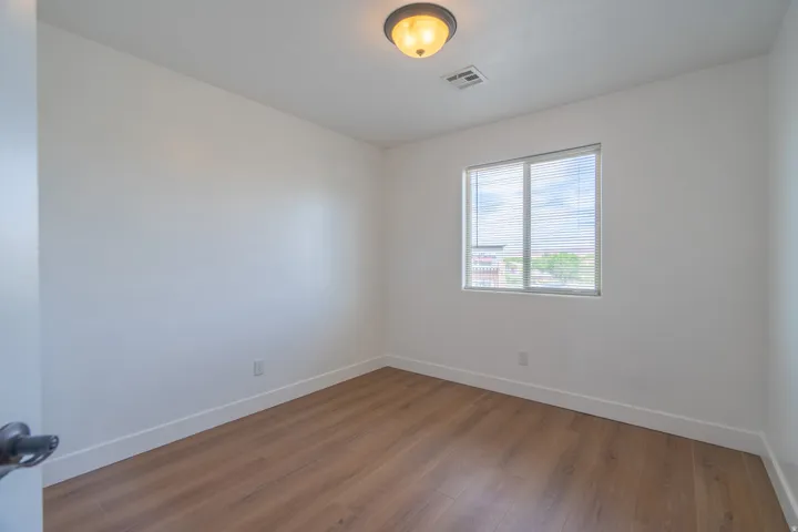 Bright interior space featuring wood-finish flooring, white walls, and a single window with blinds