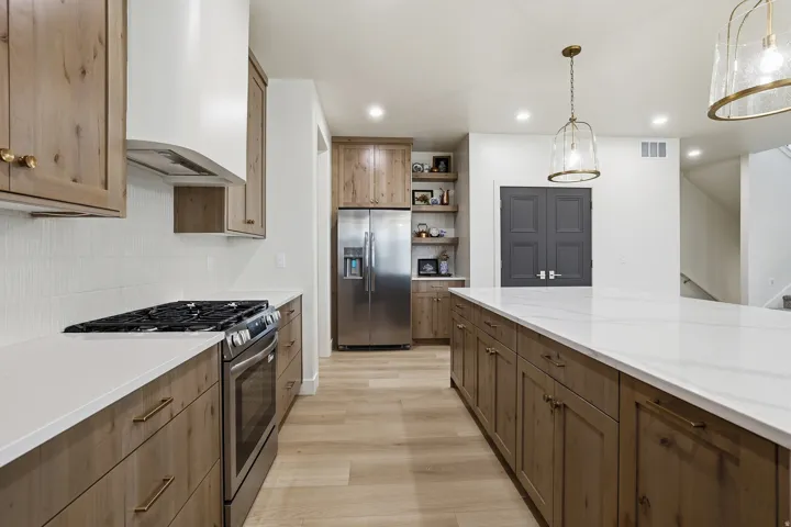 Spacious kitchen featuring an expansive island with white countertops, wood-finish cabinetry, stainless steel appliances, a gas range, and pendant lighting