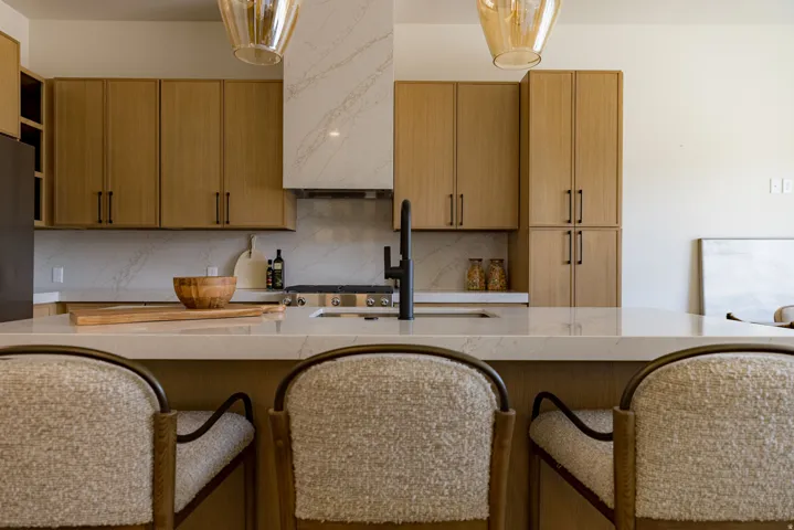 Modern kitchen featuring light wood-finish cabinetry, a large center island with seating, a gas range with a matching range hood, and light-toned countertops