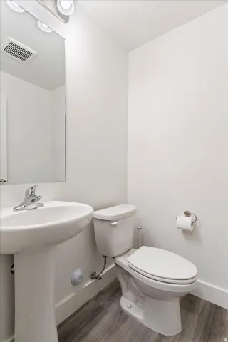 Powder room featuring a pedestal sink with chrome faucet, a white toilet, and wood-finish flooring