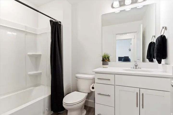 Bathroom featuring a white vanity with brushed nickel hardware, a white countertop, a rectangular mirror, and a full-size bathtub with a shower