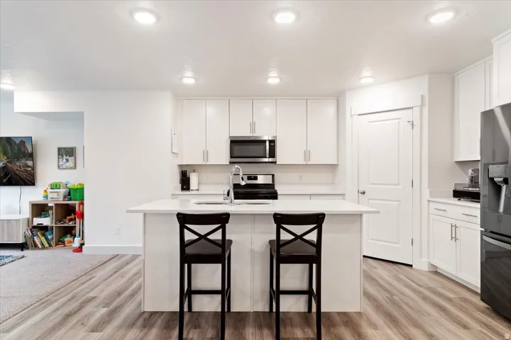 Modern kitchen featuring white cabinetry, a central island with countertop seating, stainless steel appliances, recessed lighting, and wood-finish flooring