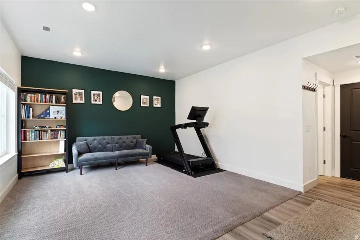Spacious room featuring a dark accent wall, recessed lighting, neutral carpeting, and wood-finish flooring at the entry