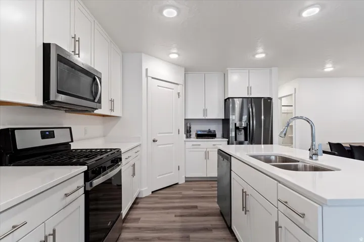 Modern kitchen featuring white shaker cabinetry, stainless steel appliances, a center island with a double sink, and wood-finish flooring