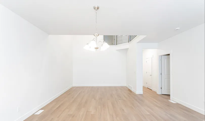 Spacious room featuring wood-finish flooring, a contemporary chandelier, white walls, and white trim