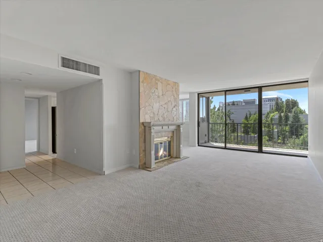 Living area featuring a stone-clad fireplace with a decorative mantel, light-toned carpet flooring, and a sliding glass door opening to a private balcony