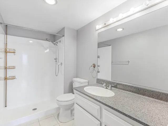 Bathroom featuring a white shower with an adjustable showerhead, a toilet, and a vanity with an integrated sink