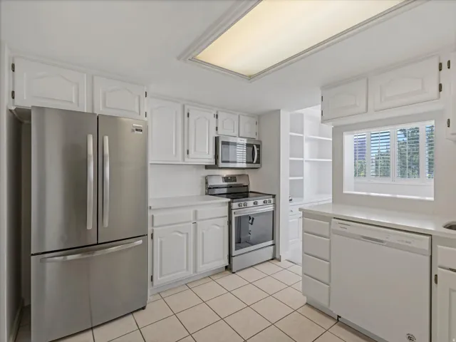 Kitchen featuring white cabinetry, quartz countertops, stainless steel appliances, tile flooring, and a pass-through window