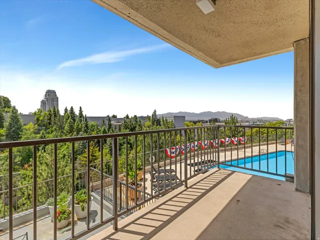 Expansive balcony with concrete flooring and a dark metal railing, overlooking a sparkling salt water swimming pool and sweeping valley and Oquirhh Mountain views