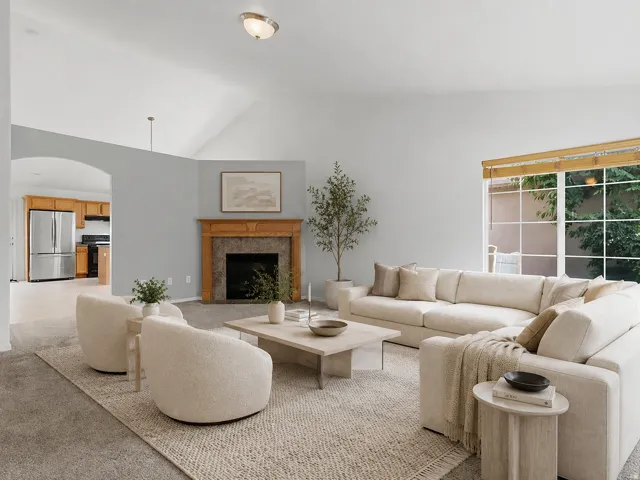 Spacious living area featuring a vaulted ceiling, a wood mantel fireplace with a stone surround, and an arched doorway leading to the kitchen