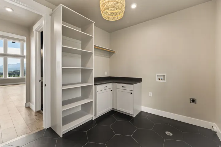 Utility room featuring hexagonal dark tile flooring, built-in open shelving, white cabinetry, dark countertops, and a clothing rod