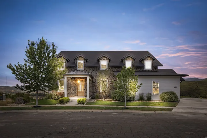 Stone and siding exterior with a covered entry, dormer windows, and a black shingle roof