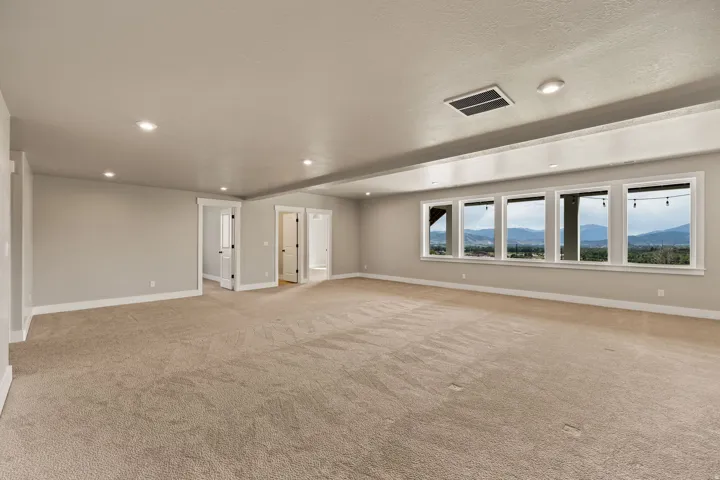 Expansive room featuring a wall of multiple windows showcasing distant mountains and a large, neutral-toned carpeted floor