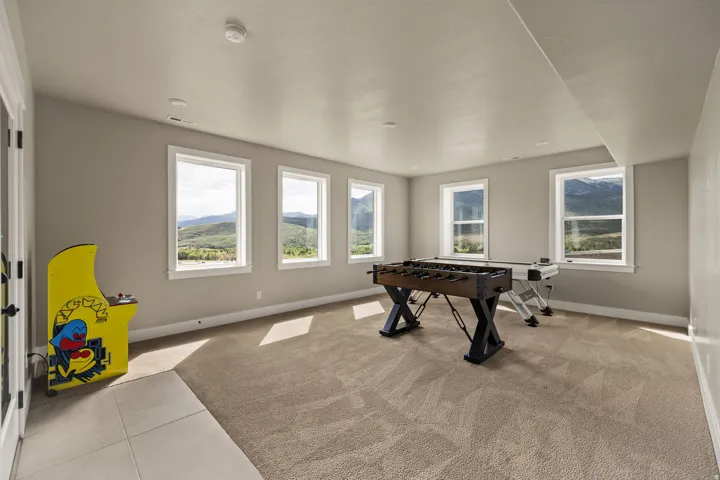 Spacious room with four large windows displaying mountain scenery, light brown carpet, and a section of light-colored tile flooring