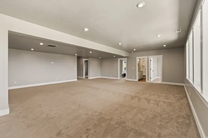 Expansive carpeted room featuring recessed lighting, multiple doorways, and a wall of windows