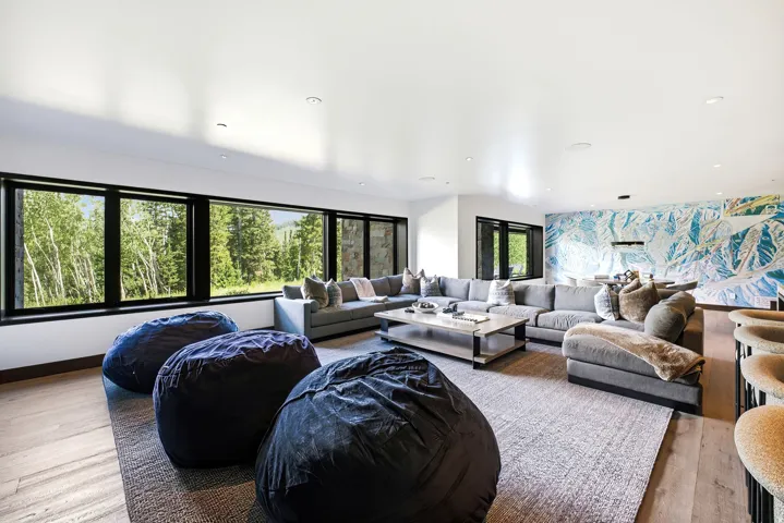 Expansive living area featuring a wall of black-framed windows, wood-finish flooring, recessed lighting, and a distinctive mural wall