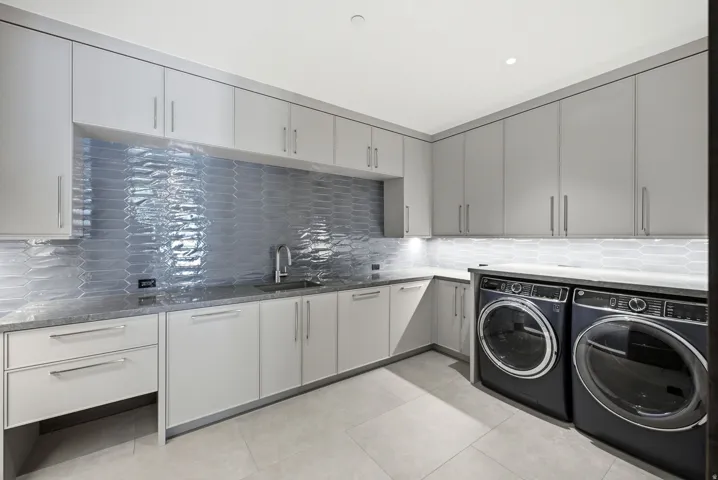 Modern laundry area featuring an under-mount sink, extensive cabinetry, light-toned tile flooring, and under-cabinet lighting