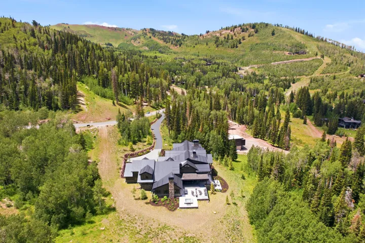 Mountainside residence featuring a multi-gabled dark roofline, stone and dark wood exterior, and an extensive outdoor patio area