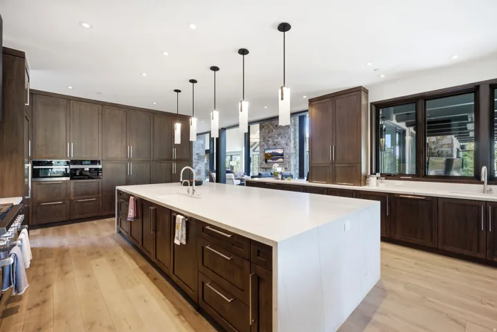 Gourmet kitchen featuring a large waterfall island with an undermount sink, pendant lighting, custom wood cabinetry, integrated appliances, and light wood-finish flooring