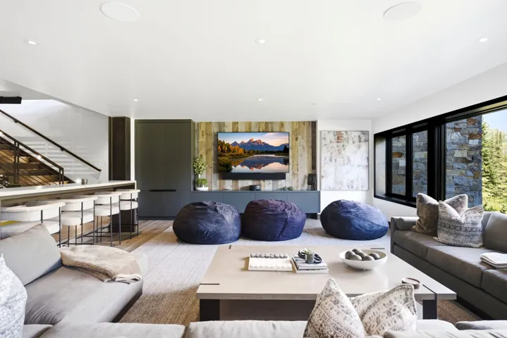 Spacious room featuring wood-finish flooring, a built-in bar with seating, a wood accent wall, and a large window with exterior stone cladding