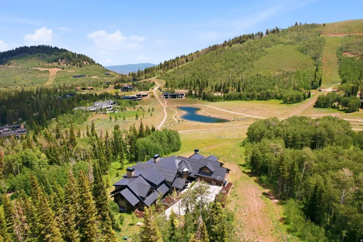 Expansive mountain property featuring a large residence with a multi-gabled roofline, surrounded by dense evergreen trees and natural landscaping