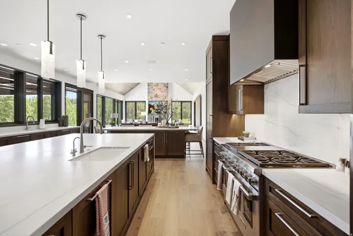 Gourmet kitchen featuring a large central island with an undermount sink, white countertops, dark wood-finish cabinetry, and stainless steel appliances, including a professional range and hood