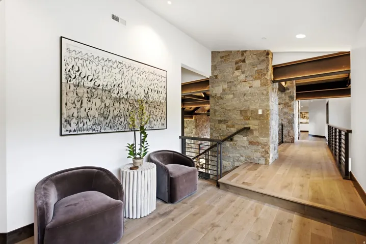Open hallway featuring natural wood-finish flooring, exposed structural beams, and stone-clad architectural elements