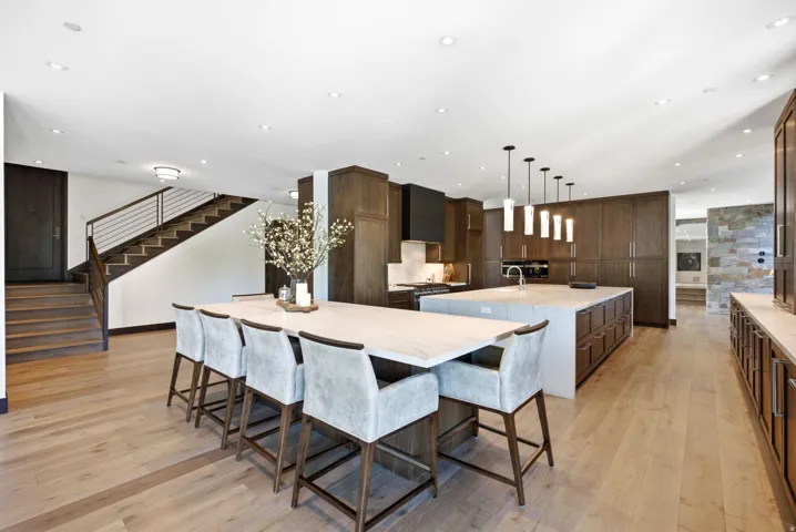 Expansive open-concept kitchen featuring two islands, light wood-finish flooring, dark wood cabinetry, and a black range hood