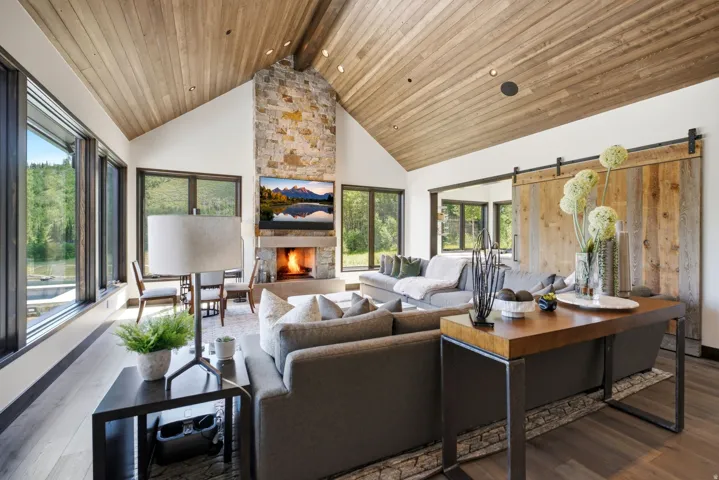 Great room featuring a vaulted wood-finish ceiling, a stone fireplace with a built-in hearth, and expansive windows
