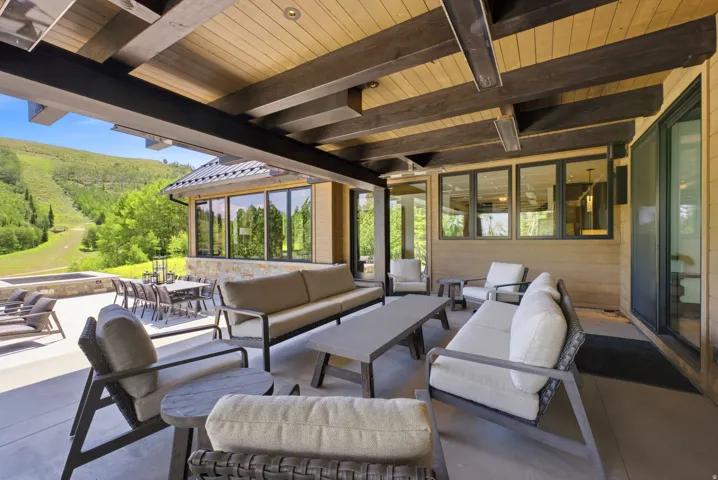 Expansive covered patio featuring a wood-finish ceiling with exposed beams, recessed lighting, and a stone-clad hot tub