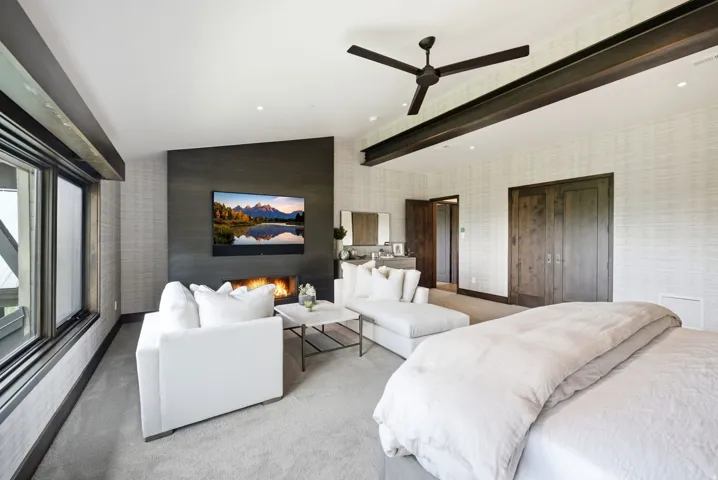 Spacious room featuring a linear fireplace, dark wood-tone accent wall, large windows, ceiling fan, and exposed ceiling beam