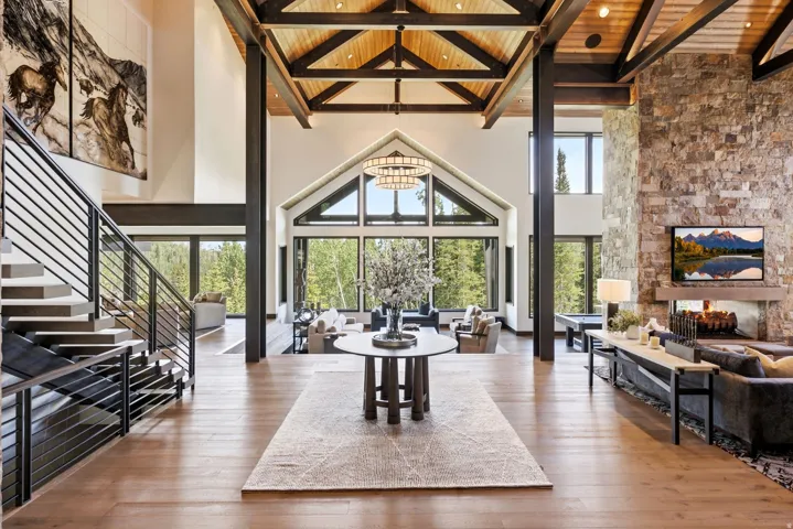 Grand foyer featuring wood-finish flooring, a contemporary staircase with metal railings, and a vaulted ceiling with exposed wood beams