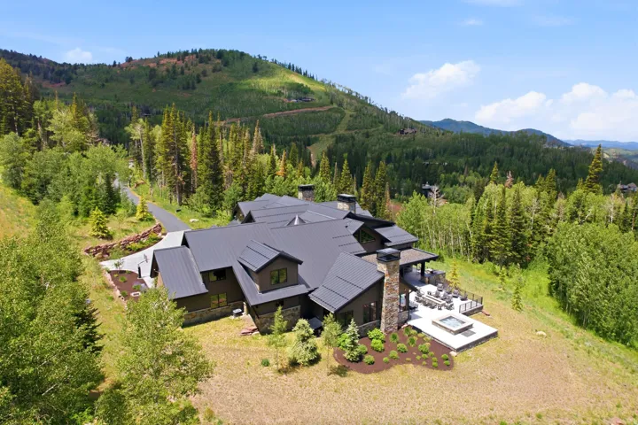 Contemporary mountain residence featuring a dark metal roof, stone and wood-paneled exterior, and multiple chimneys