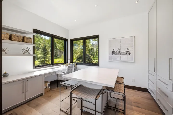 Home office featuring extensive built-in cabinetry, wood-finish flooring, and multiple windows with dark frames