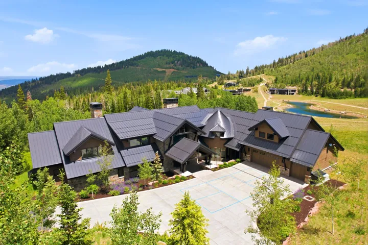 Spacious modern residence featuring a multi-gabled metal roof, stone and wood exterior, and an expansive paved motor court