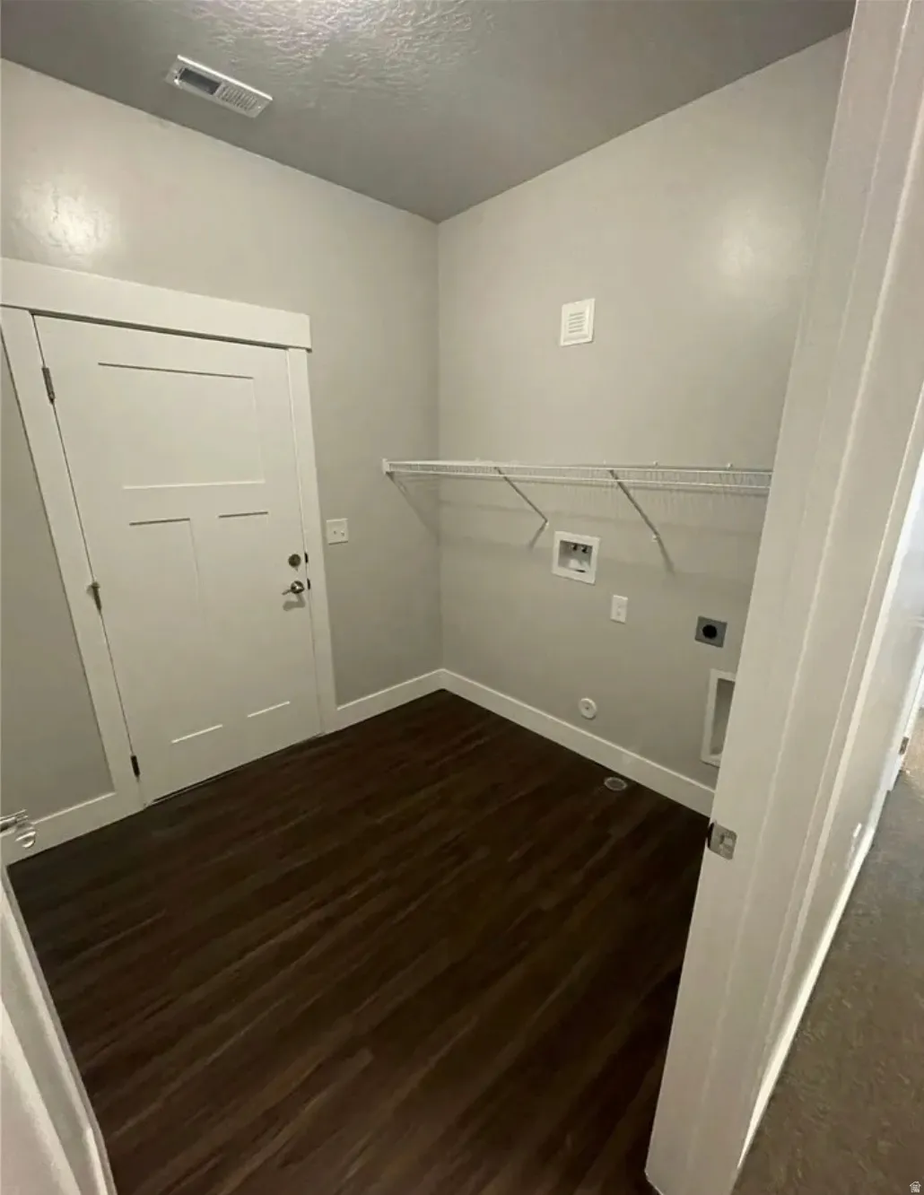 Dedicated laundry area featuring dark wood-finish flooring, light gray walls, a white wire shelf, and modern white trim