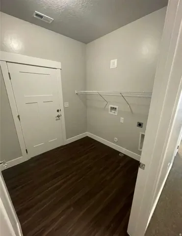 Dedicated laundry area featuring dark wood-finish flooring, light gray walls, a white wire shelf, and modern white trim